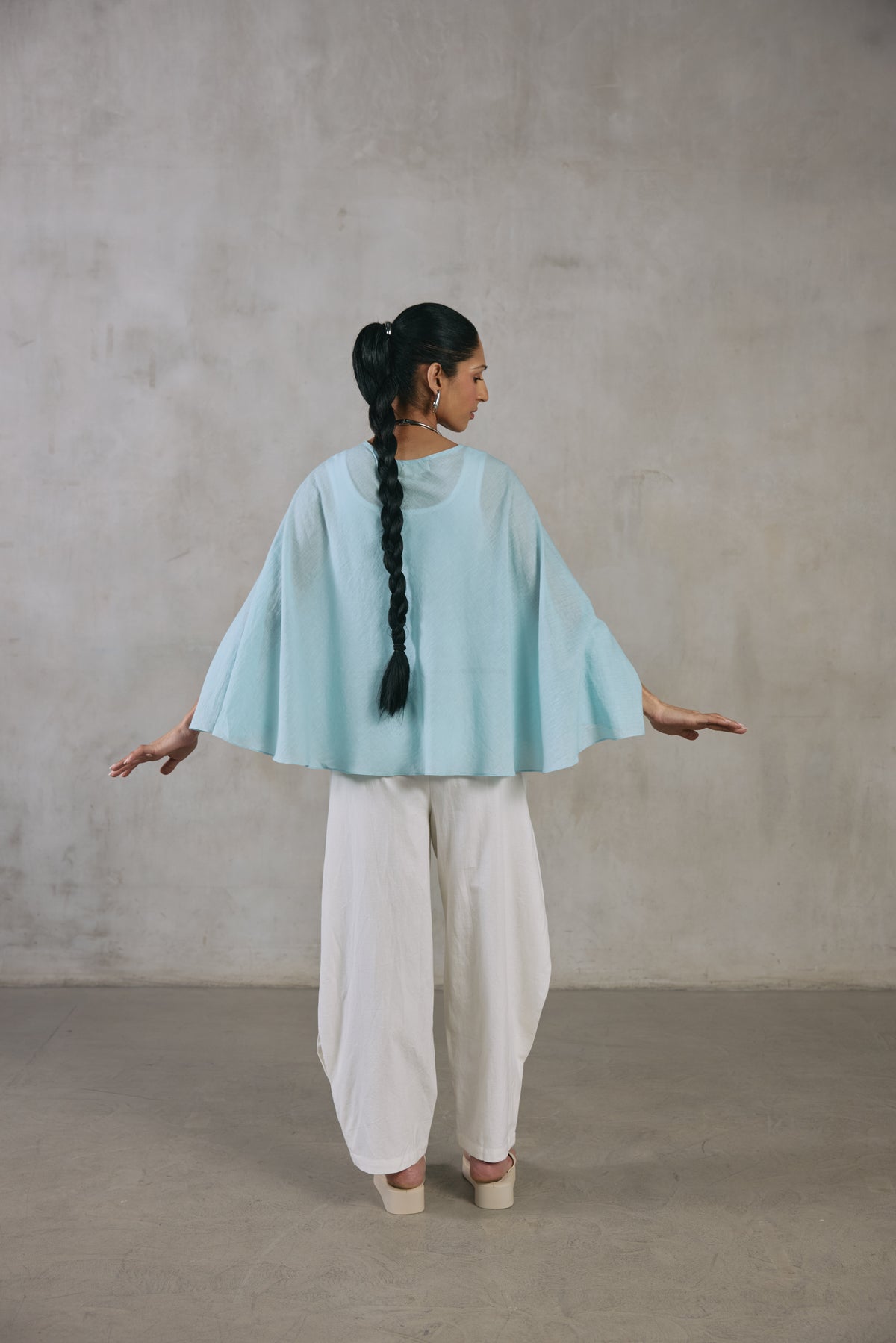 Model in the light blue cape poncho over ecru wide-leg pants
