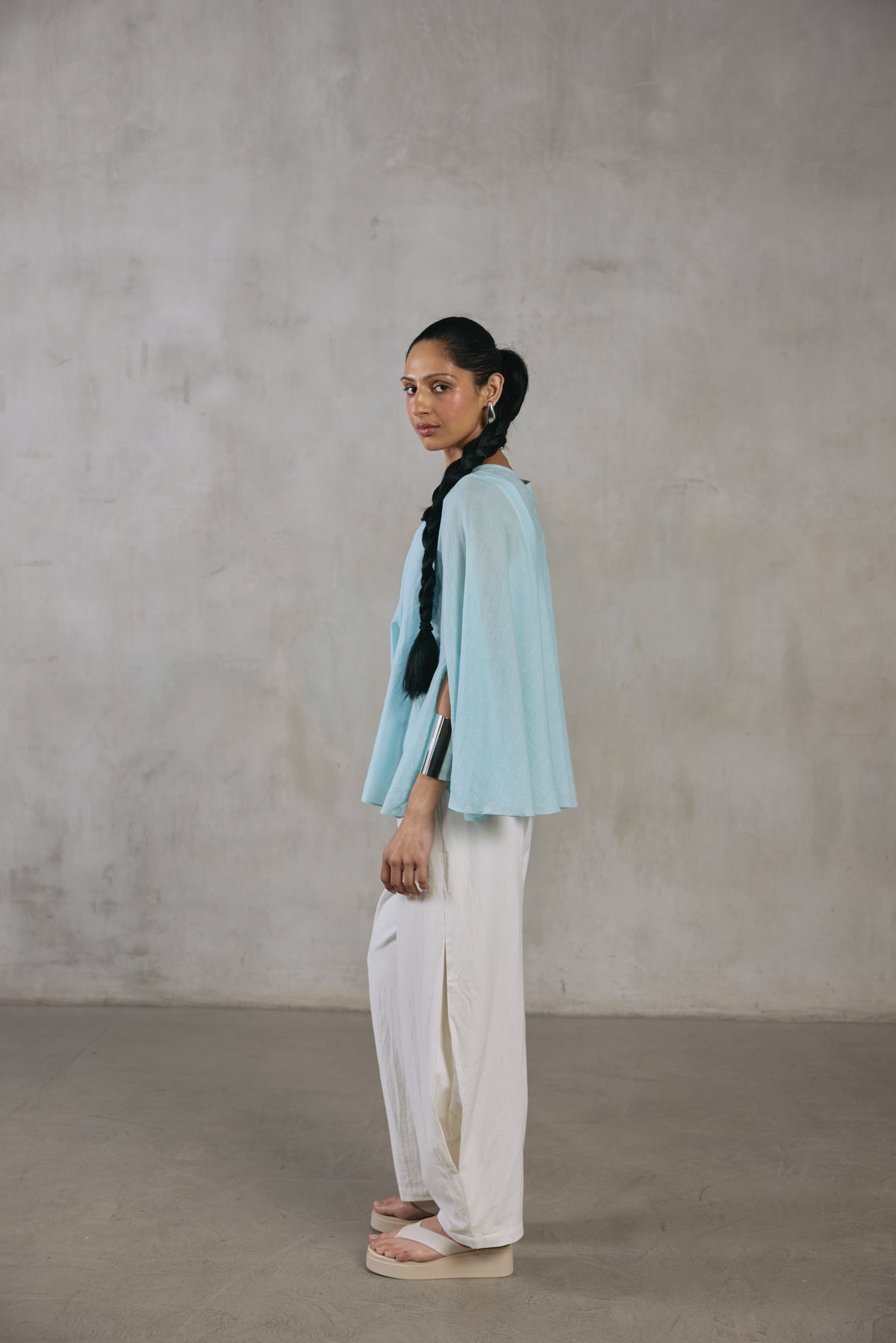 Side view of the light blue cape poncho over ecru pants