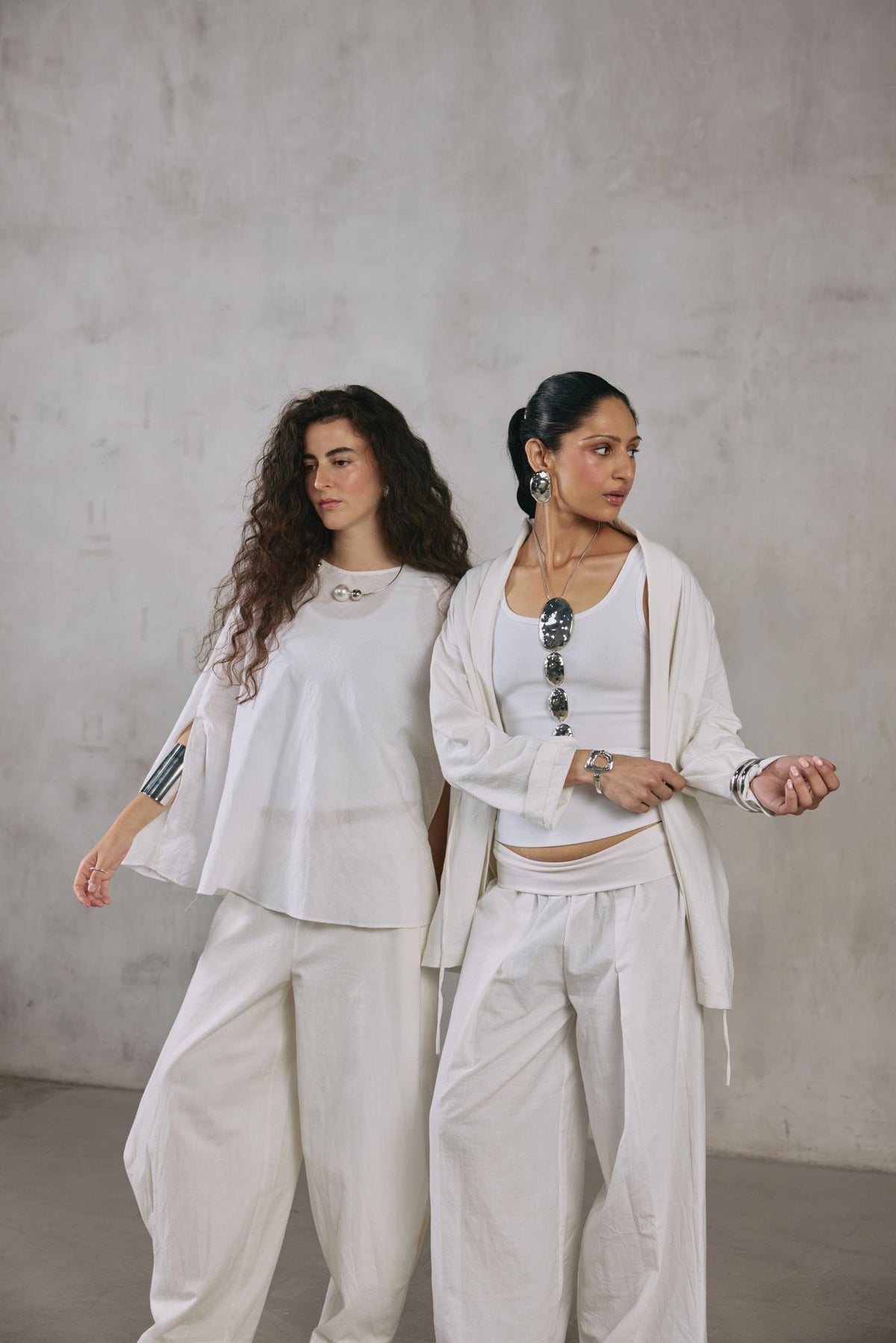 Two women in ecru Khadi against a plaster wall