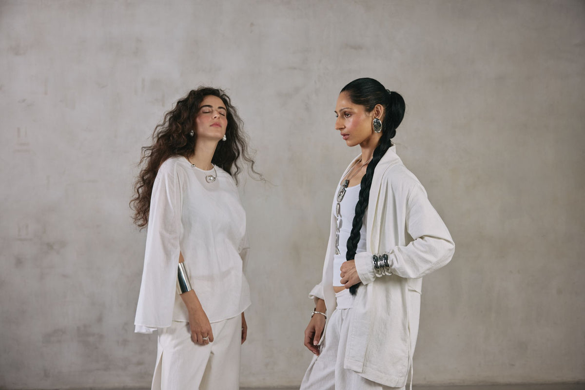 Two women in ecru Khadi against a plaster wall